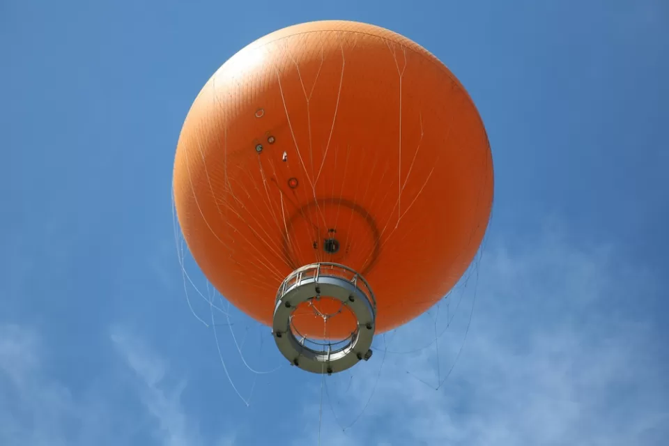 View from below of orange tethered hot-air balloon floating in blue sky